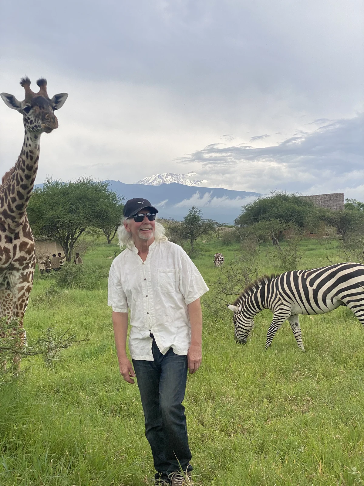 Brian in Tanzania beside a giraffe and zebra, with Mount Kilimanjaro in the background