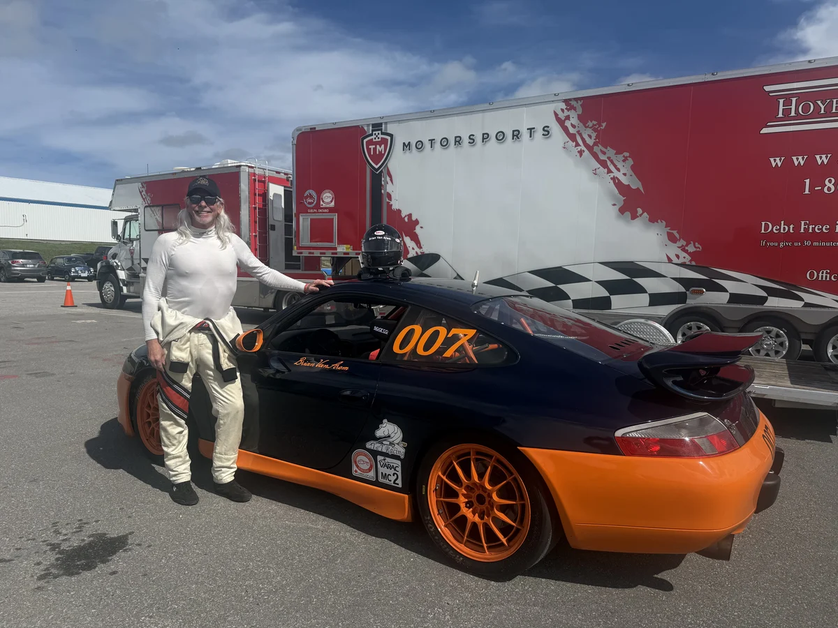 A driver beside a black and orange Porsche